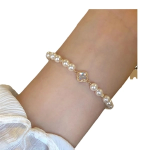 Elegant baroque pearl bracelet with gold clover charm on woman wrist, minimalist style
