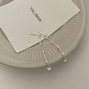 Close-up of silver long tassel earrings with delicate heart pendants on a ceramic tray
