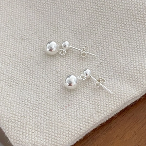 Detailed close-up of minimalist double silver ball stud earrings on textured beige linen