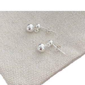 Polished silver double ball drop earrings with minimalist round spheres on fabric background