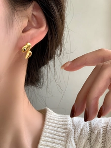 Dettaglio di un elegante orecchino a perno dorato a spirale indossato da una modella