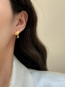 Primo piano di un orecchino d'oro minimalista con forma irregolare indossato da una modella
