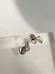 Dettaglio degli orecchini d'argento astratti con design fluido e finitura a specchio