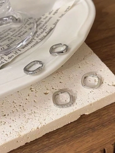 Close-up of four silver geometric square hoop earrings with polished and zircon details