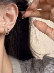 Close-up of elegant square zircon and polished silver hoop earrings set worn by a model