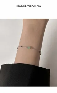 Detail of silver chain bracelet with green jade bead and star charm on woman wrist