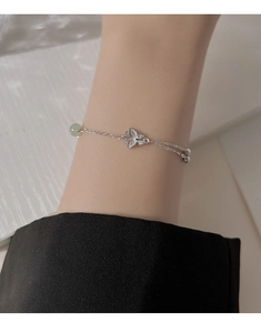 Macro detail of silver butterfly bracelet with a light green jade-like bead on wrist