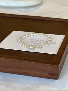 Detail of elegant pearl bracelet with golden clover charm on a wooden display