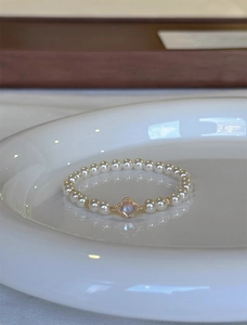 Detail of white pearl bracelet with gold clover charm on a white ceramic plate