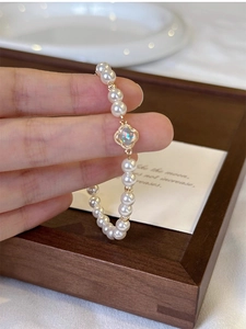 Detailed shot of white pearl bracelet with gold clover pendant and opal inlay