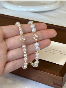 Detail of white pearl bracelet featuring a gold clover motif worn on the wrist