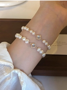 Detail shot of dual-layered pearl bracelets featuring golden clover charms on a wrist