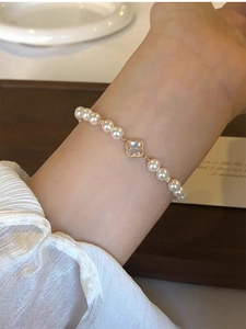 Detail of white pearl bracelet with gold clover charm on a woman's wrist