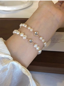 Detail of layered baroque pearl bracelets with golden clover charms on a wrist
