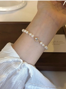 Detail of elegant pearl bracelet with gold clover charm on a female wrist
