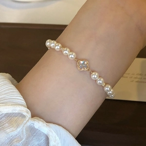 Elegant white pearl bracelet with a golden clover pendant worn on a female wrist
