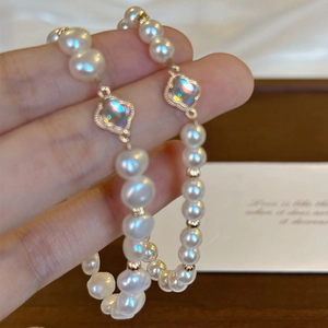 Elegant white pearl bracelet featuring iridescent clover charms on a warm background