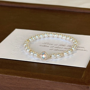 Elegant pearl bracelet featuring a gold clover charm with iridescent stone on wood