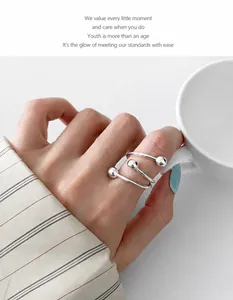 Detail of silver spiral bead ring on finger holding a minimalist white ceramic cup