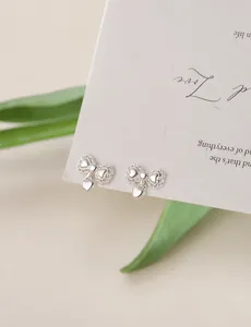 Close-up of silver bow stud earrings with heart pendants on a textured display card