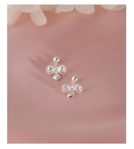 Close-up of silver bow stud earrings with heart charms and screw back on pink silk