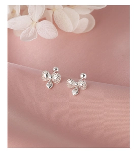 Close-up of silver bow stud earrings with heart pendants on soft pink silk fabric