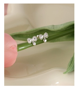 Detail of silver bow earrings with hanging heart charms on a tulip flower stem