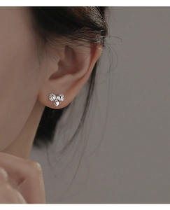 Silver bow stud earring with heart charm detail shown on a model's ear in close-up