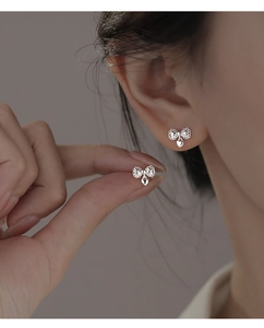 Close-up of silver bow stud earrings with small heart pendant held between fingers