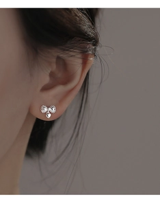 Close-up of a silver bow and heart earrings with intricate lace-like hollow textures