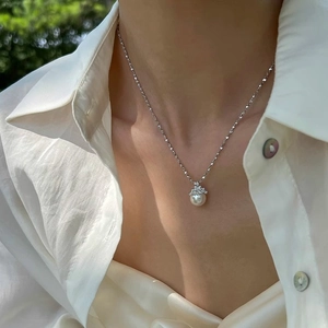 Collier élégant avec perle et pendentif couronne porté par un mannequin en extérieur