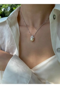 Gros plan du collier à pendentif perle couronne porté sur une chemise en lin blanc
