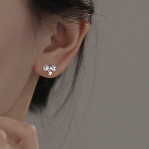 Elegant silver bow stud earrings with heart pendant shown on model ear profile
