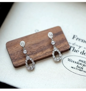 Macro shot of silver teardrop earrings with zircons on a wooden jewelry display