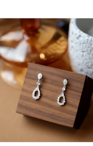 Detail of drop-shaped hollow earrings with white zircon on a wooden display stand