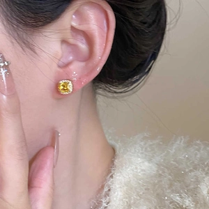 Close-up of yellow cushion-cut zircon halo stud earrings worn with a white knit outfit