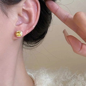 Macro detail of square yellow gemstone halo earrings worn on the ear for a stylish look
