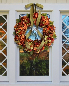 Detail of fall hydrangea wreath with orange petals and a green burlap bow on a window