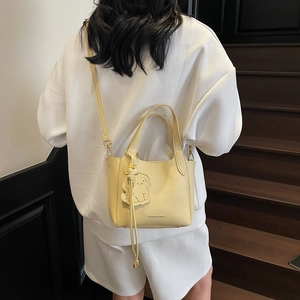 Light yellow lychee leather bucket bag with top handle and puppy charm on model
