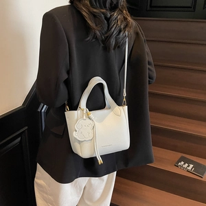 Chic creamy white leather bucket bag with puppy charm shown on a wooden staircase