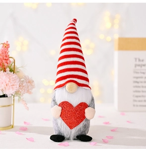 Macro shot of a Valentine gnome doll holding a red glitter heart with striped knitted hat