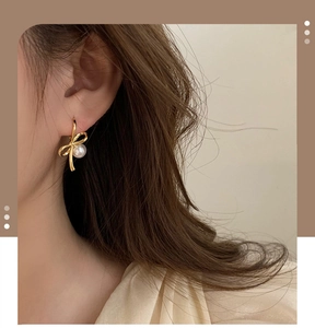 Détail de boucles d'oreilles nœud doré avec perle portées par un mannequin élégant