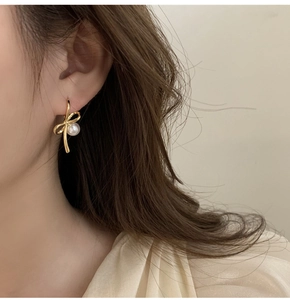 Gros plan de boucles d'oreilles nœud doré avec perle sur modèle pour un look chic
