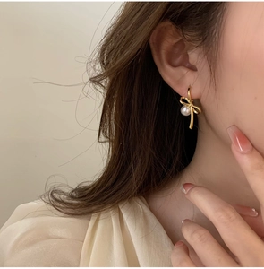 Détail d'une boucle d'oreille nœud doré avec perle blanche portée par une femme