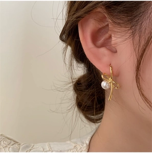 Détail de boucles d'oreilles nœud dorées avec perle blanche sur le mannequin