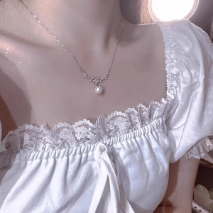 Detail eines blumenförmigen Diamantanhängers mit weißer Perle an einer feinen Silberkette