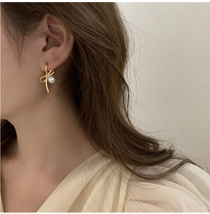 Gros plan de boucles d'oreilles nœud doré avec perles blanches portées par un modèle