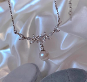 Makroaufnahme einer silbernen Blumen-Halskette mit Pavé-Zirkonia und hängender weißer Perle