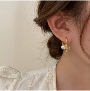 Détail d'une boucle d'oreille nœud doré avec perle ronde portée par un mannequin