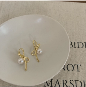 Gros plan de boucles d'oreilles nœuds dorés avec perles blanches sur un plat en céramique